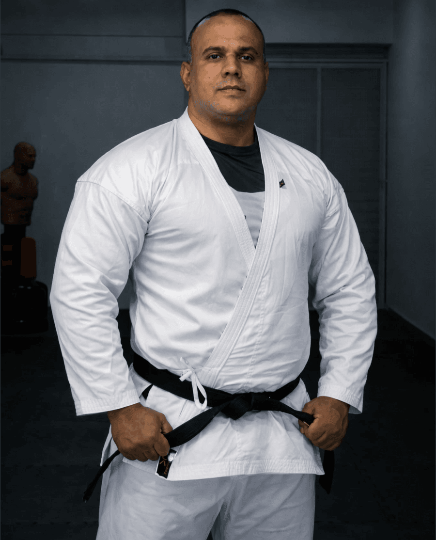 Sensei Caio Rodrigo, professor da EKG, em pé olhando para a frente, de kimono (gi) branco e faixa preta.